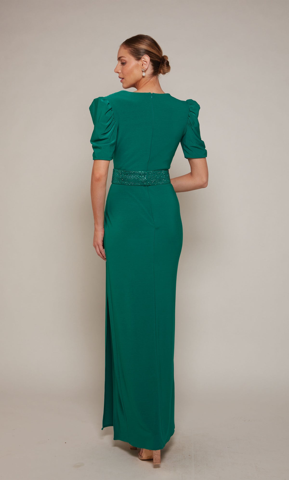 An emerald evening gown with puff sleeves, a closed zipper back, an embellished belt, and elegant side slit.