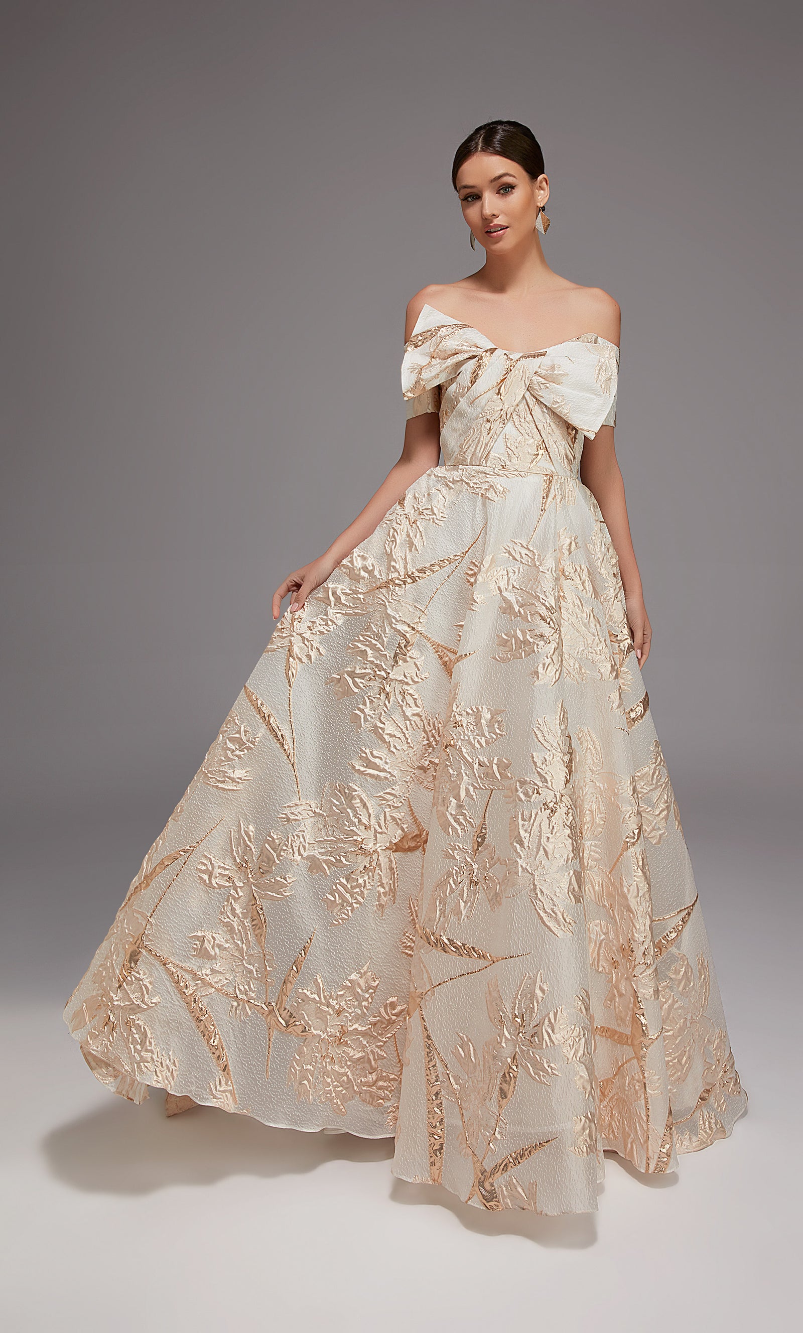 Woman in a white lace dress sitting on a gold couch in an elegant room with a chandelier.