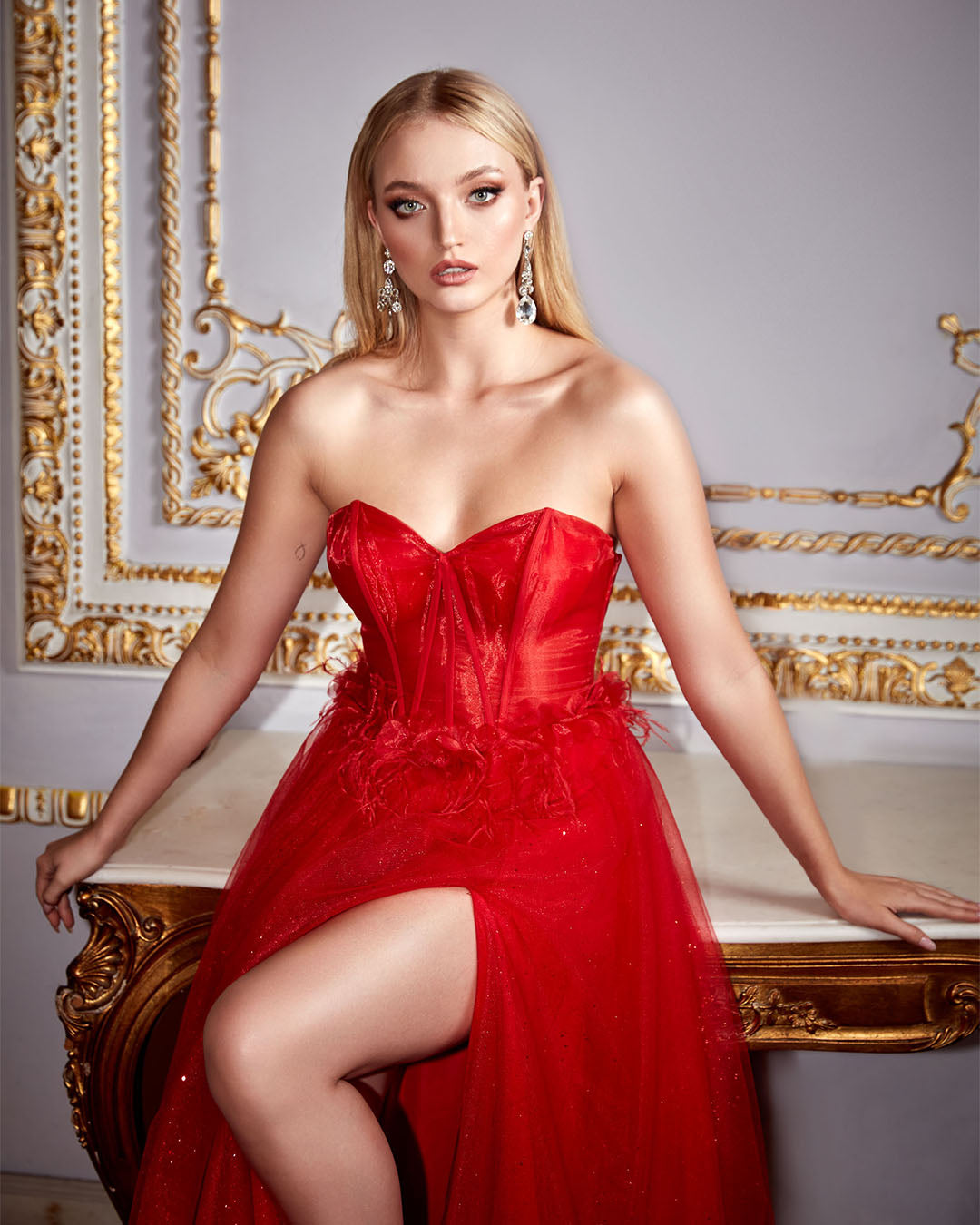 Strapless red corset prom dress with feather accents and high side slit.