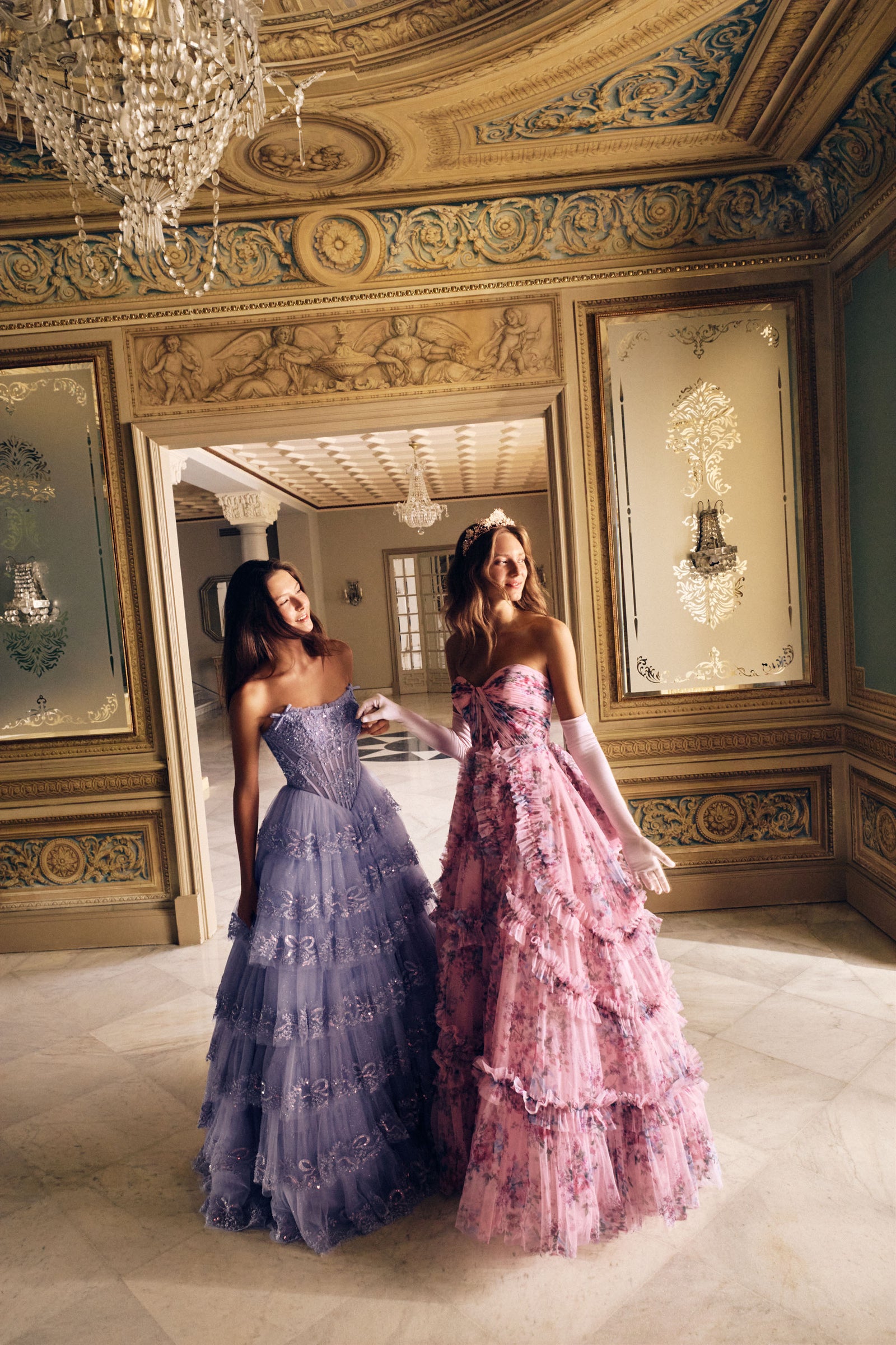Two women in elegant dresses standing in an ornate room.