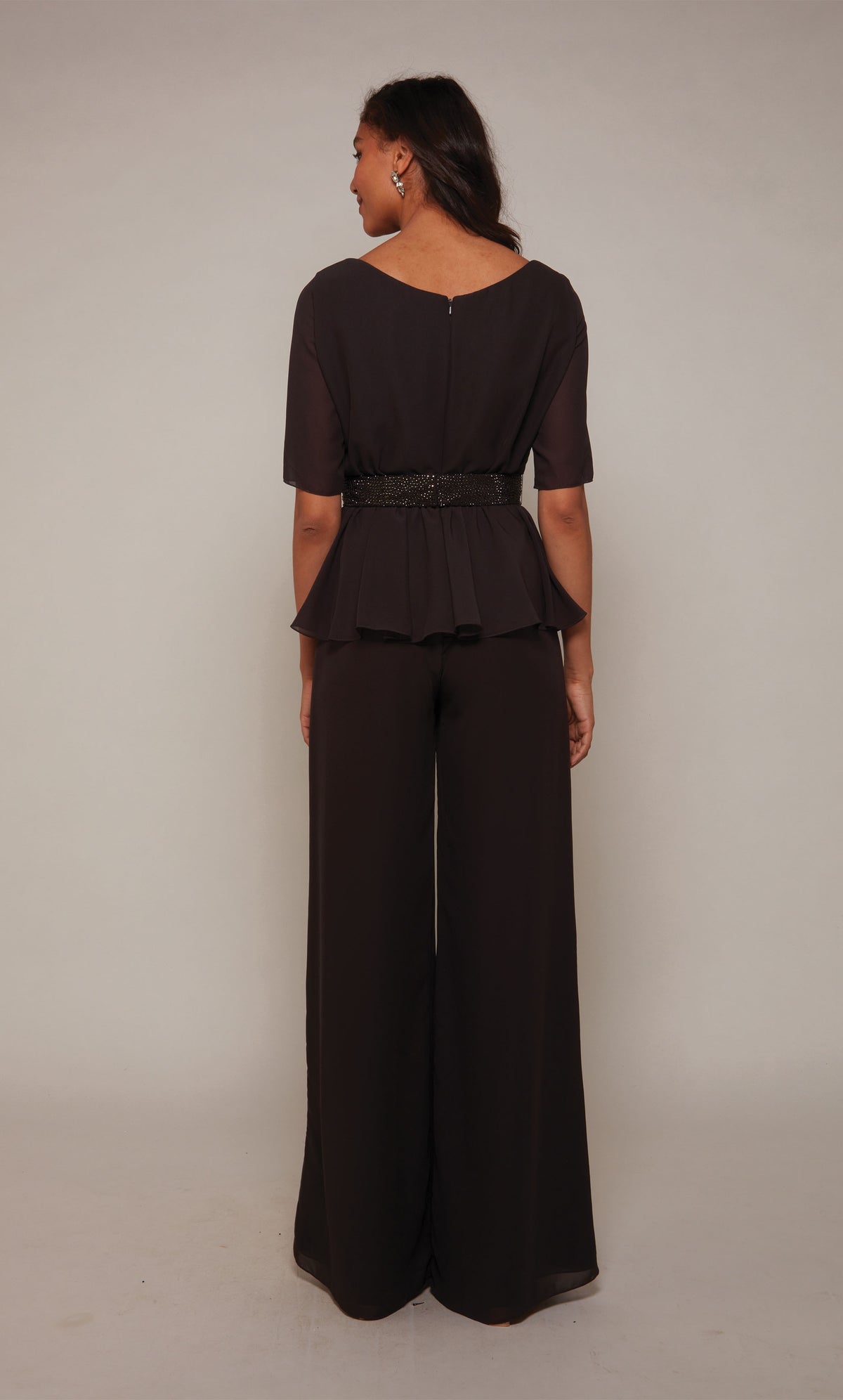 A peplum formal jumpsuit with short sleeves, an closed zipper back, an faux beaded belt at the waistline and wide leg pant in charcoal.