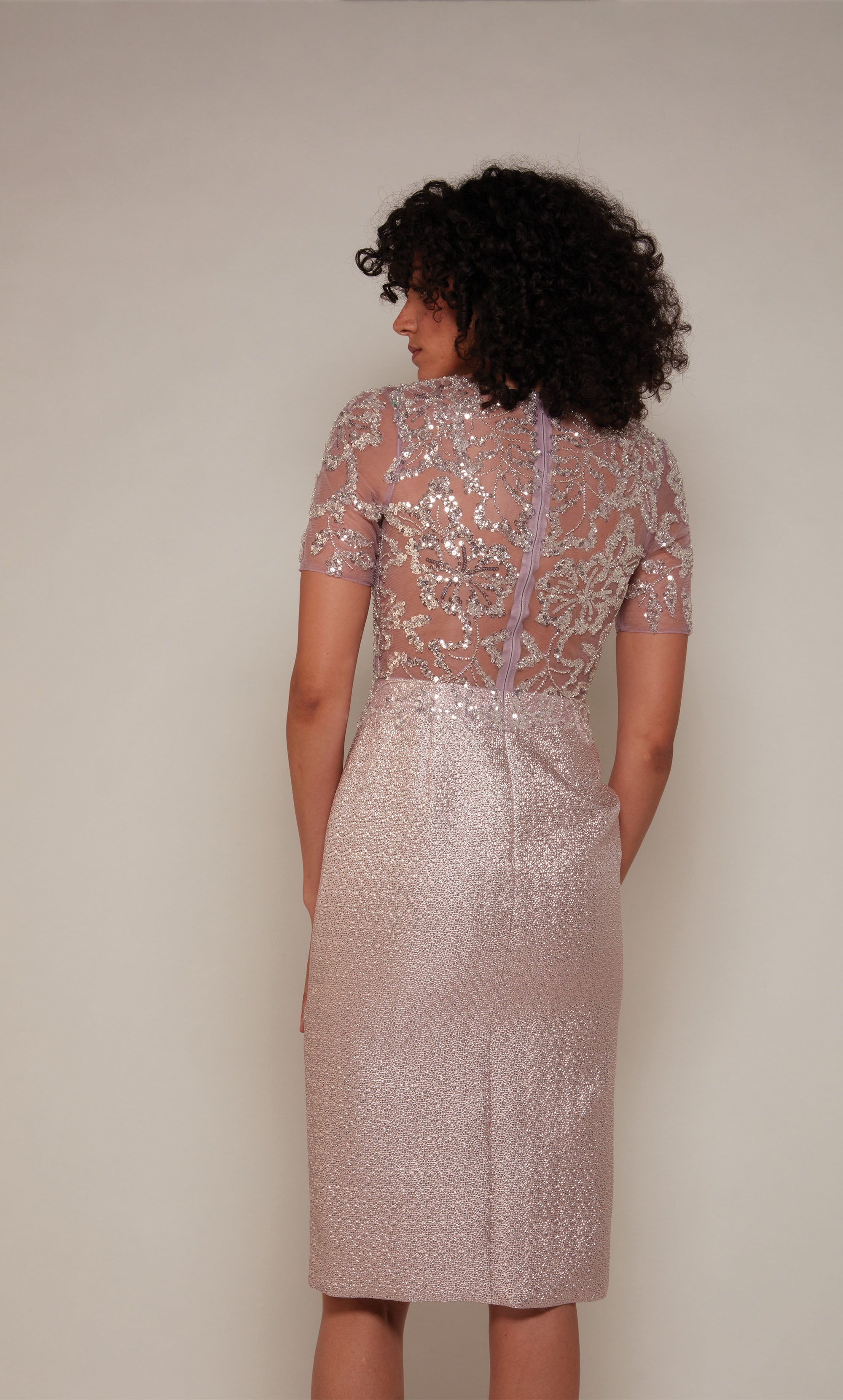 A knee length mother of the bride dress with an illusion neckline and short sleeves in a light pink colored Jacquard.