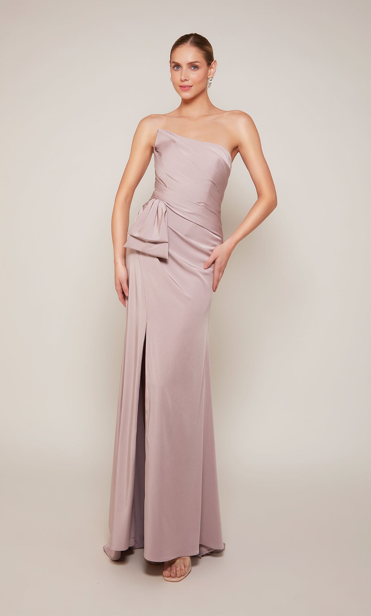 A strapless designer gown highlighting a pleated bodice, a bow at the waistline, and a side slit in the color rosewood.