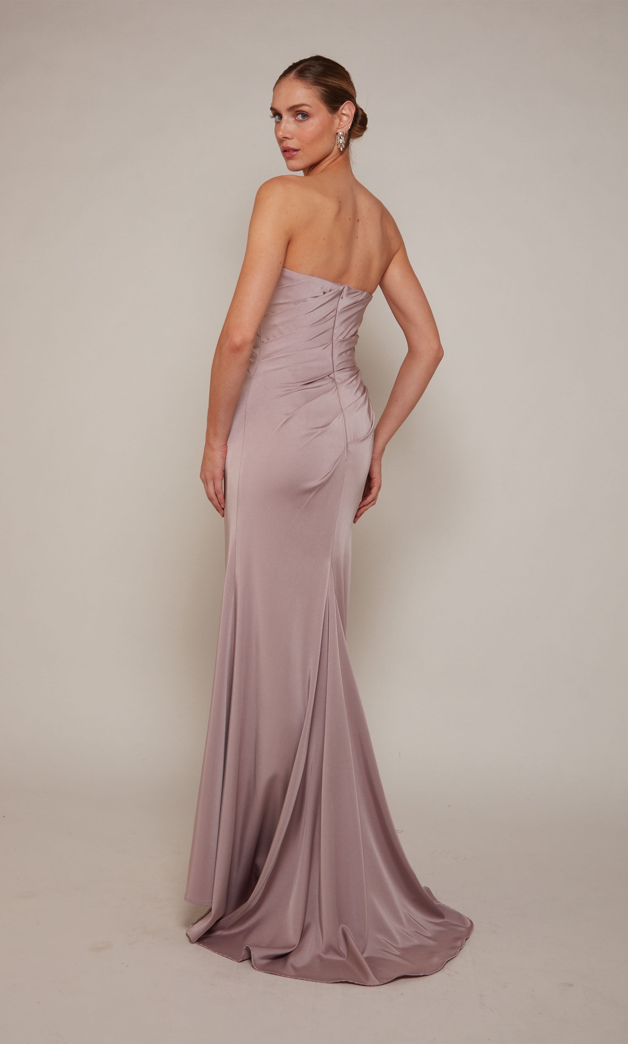 A strapless designer gown highlighting a pleated bodice, a bow at the waistline, and a side slit in the color rosewood.