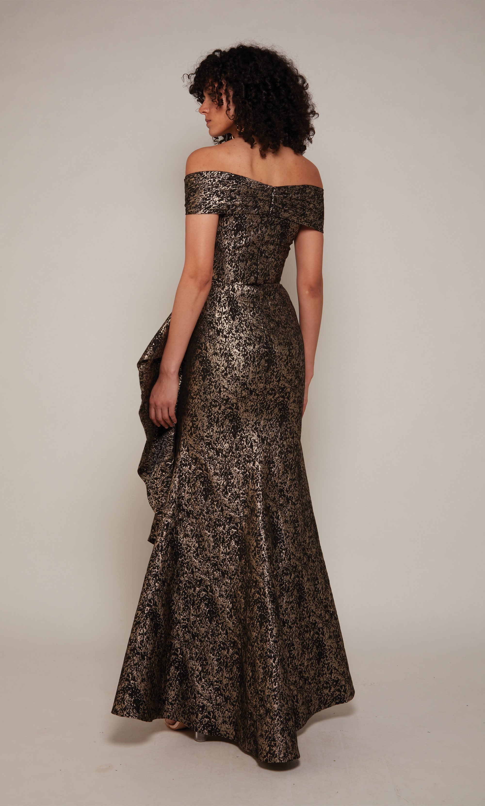 A black and gold Jacquard formal gown with an off the shoulder, twist neckline and a cascading side ruffle.