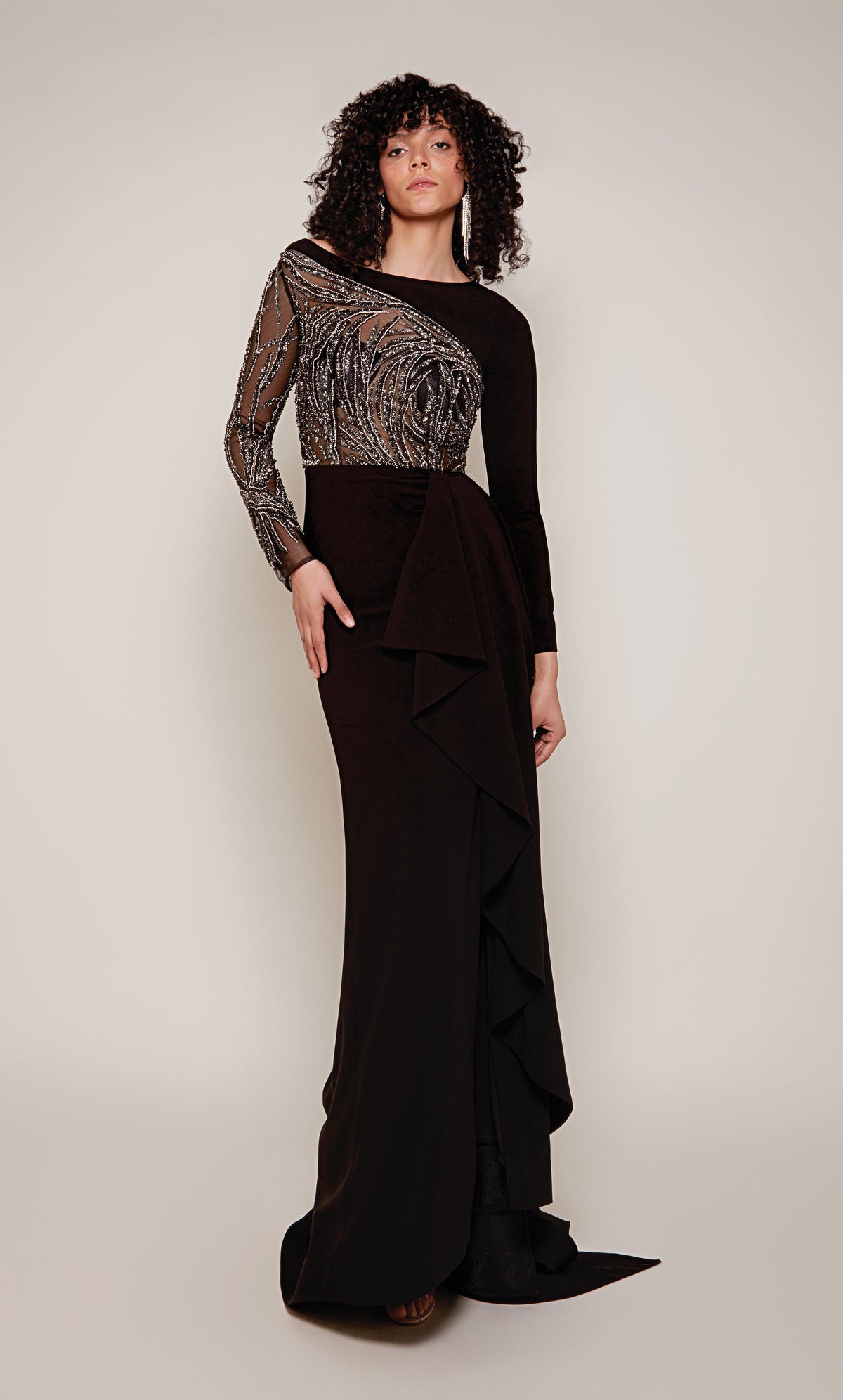 A long sleeve evening gown with a sheer, embellished bodice and sleeve and a cascading ruffle in classic black with silver accents.