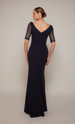 A long navy wedding guest dress with a V-shaped back, short embellished sleeves, and a fitted skirt that flares slightly from the knee to the bottom of the hemline.