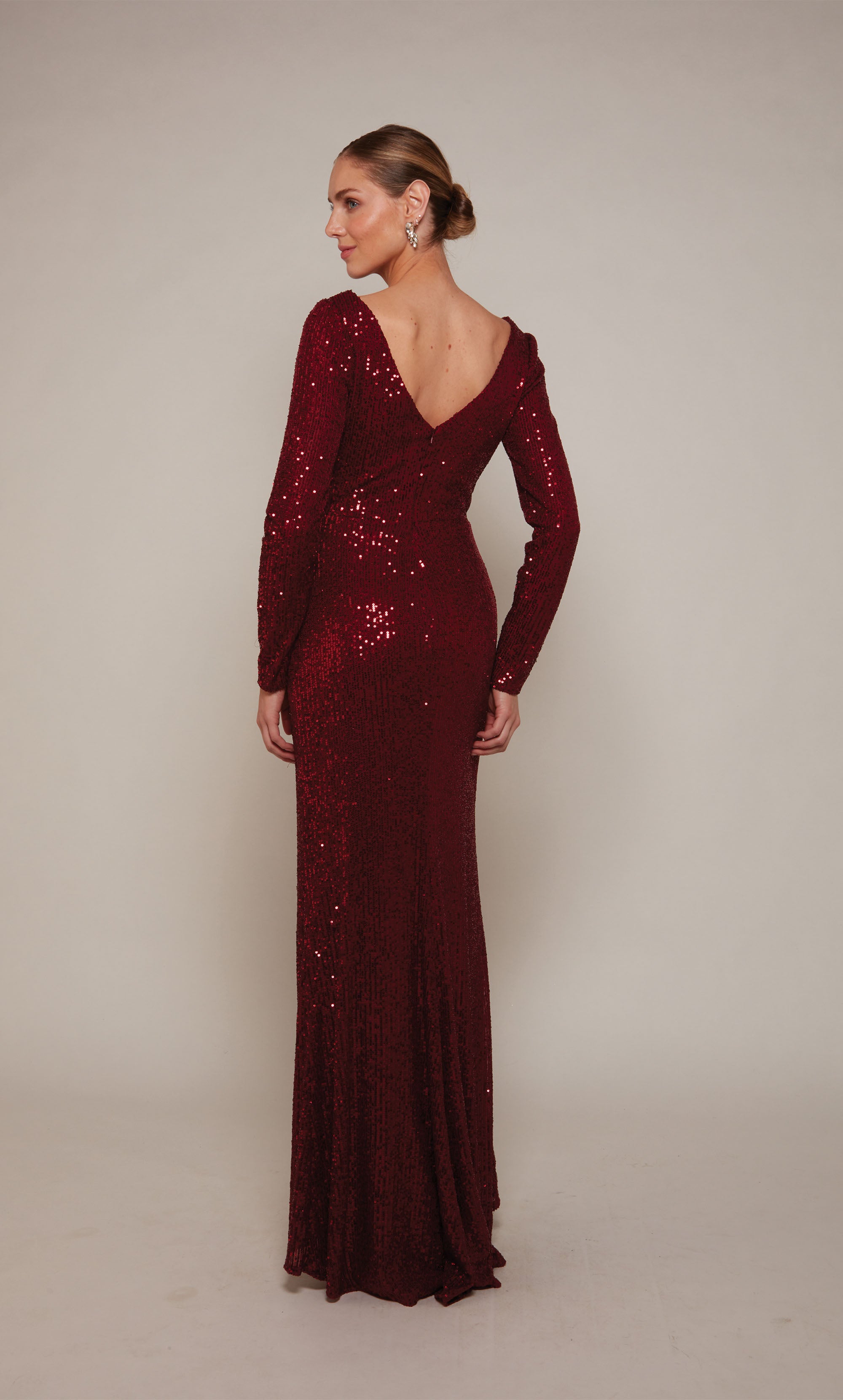 A long sleeve designer gown with a V-neckline, draped bodice, and side slit crafted from a rich wine colored sequin fabric.