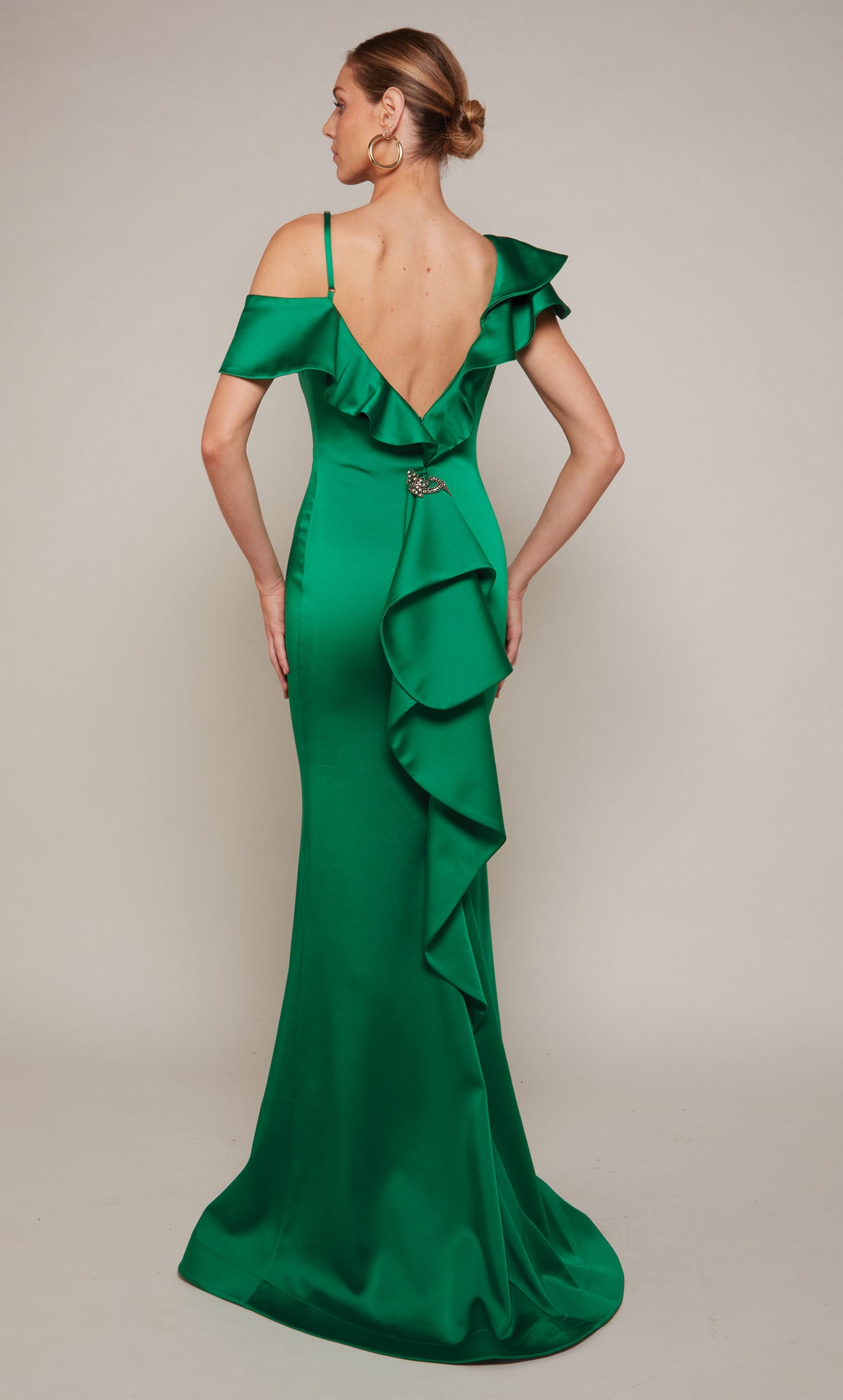 A satin formal dress with a V-shaped open back, ruffle detail, and a slight train in emerald green.