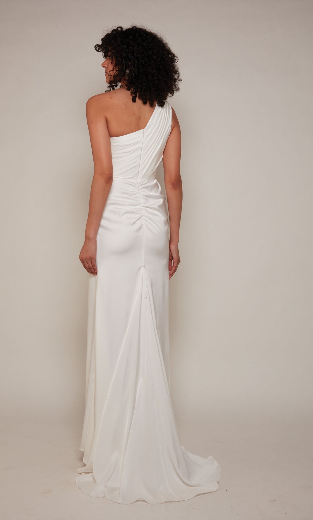 An elegant, satin one shoulder gown with ruching detail, a closed zipper back, and train in the color diamond white.