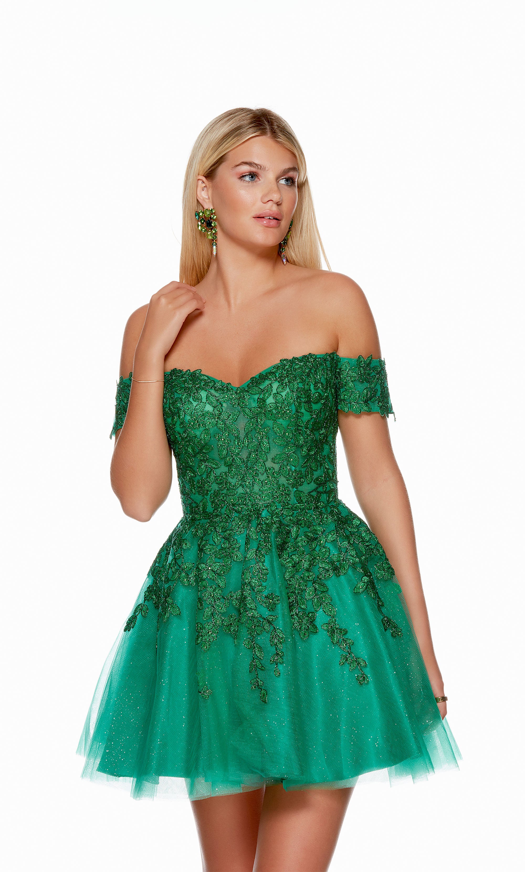 A playful emerald green short party dress featuring an off the shoulder neckline, a sheer bodice adorned with floral lace appliques, and a glitter-tulle skirt.