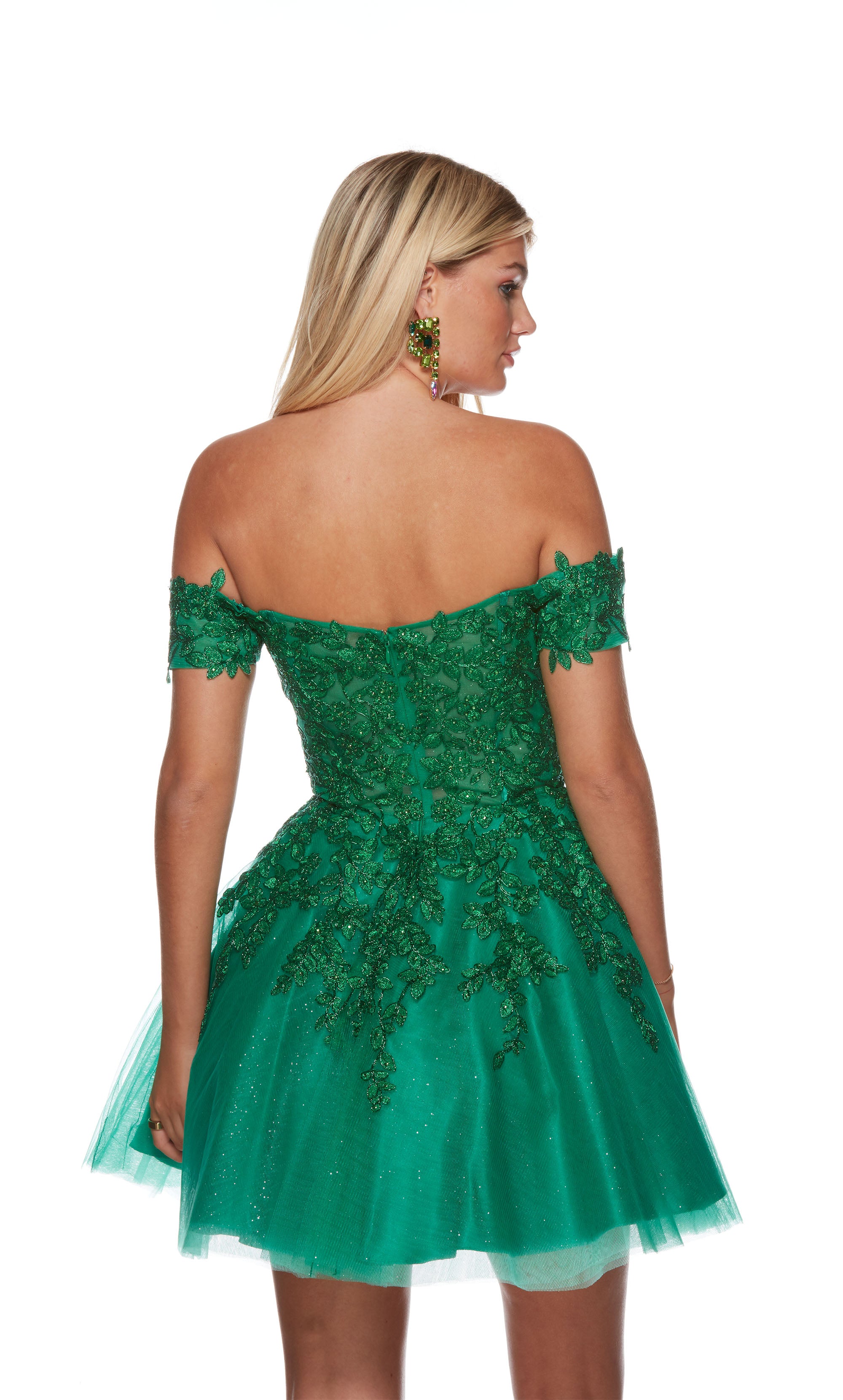 A playful emerald green short party dress featuring an off the shoulder neckline, a sheer bodice adorned with floral lace appliques, and a glitter-tulle skirt.