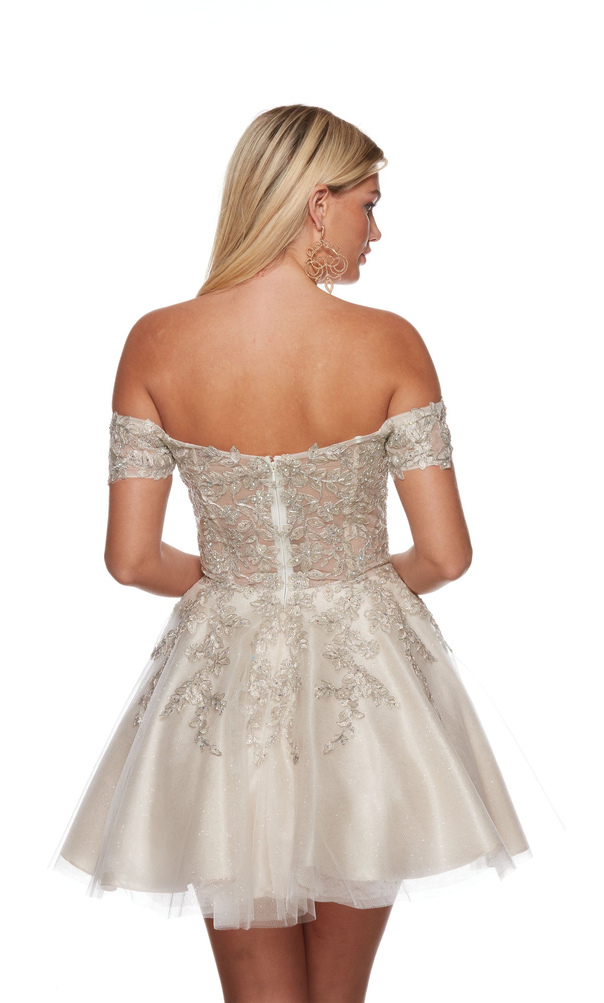 A playful ivory-champagne colored short party dress featuring an off the shoulder neckline, a sheer bodice adorned with floral lace appliques, and a glitter-tulle skirt.