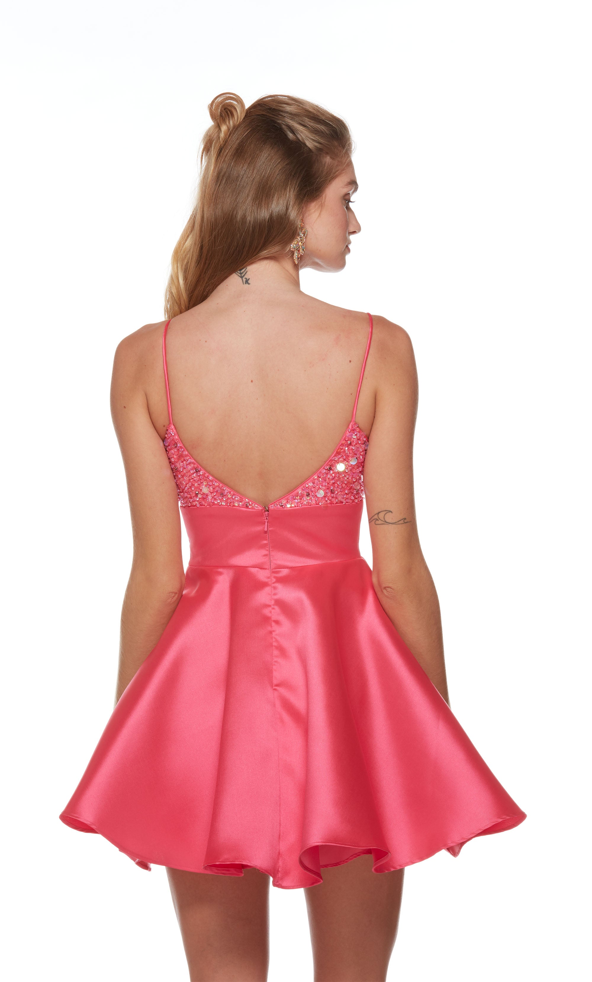 A playful hot pink homecoming dress, featuring a soft V neckline, an open V shaped back, and a flared skirt. The top of the dress is embellished with iridescent beads for a touch of sparkle.