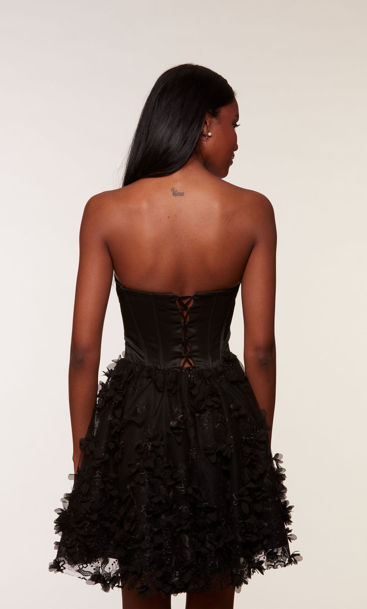 A black strapless satin corset dress, showcasing a fitted lace-up back bodice and a flared skirt adorned with intricte 3D flowers.