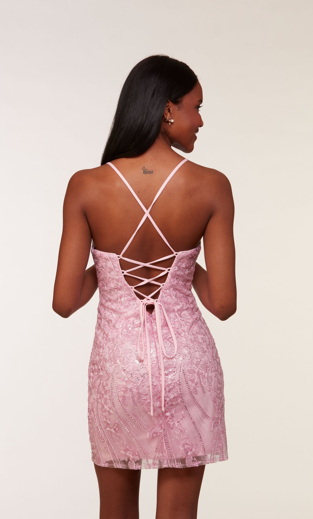 A pink, sleeveless short formal dress with a lace-up back and fitted silhouette. It features a pretty floral lace overlay and heat-set stones for a little sparkle.
