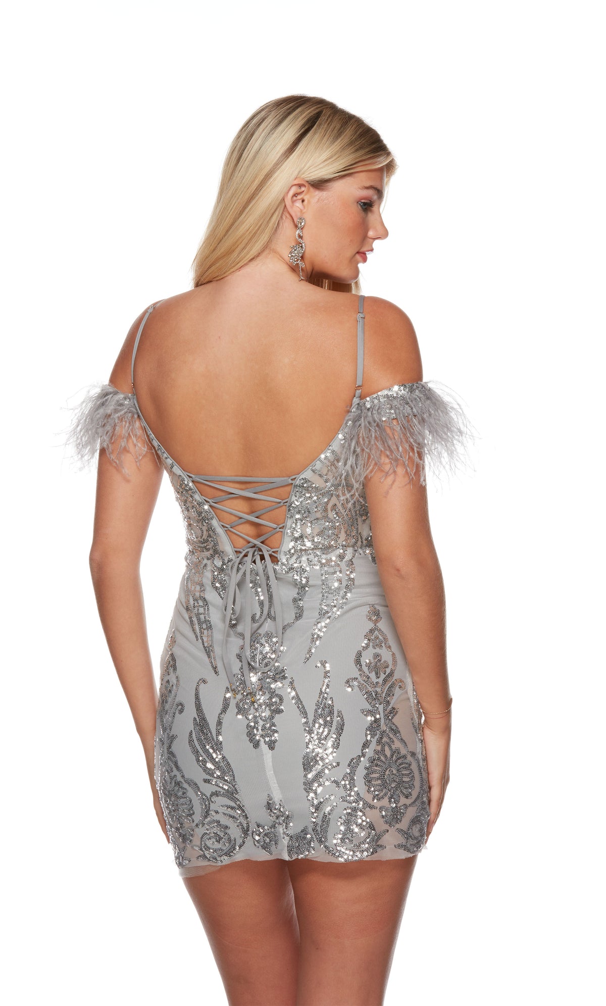 A fitted short silver homecoming dress highlighting an off-the-shoulder neckline, a lace-up back, and an intricate sequin embellished design throughout.