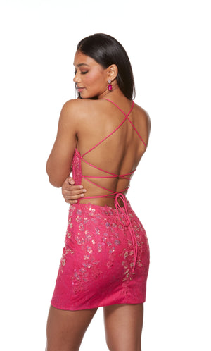 A striking electric fuchsia-colored short corset dress highlighting a strappy open back and sheer bodice. The lace overlay and sequin detailing add the perfect touch to finish off the look.