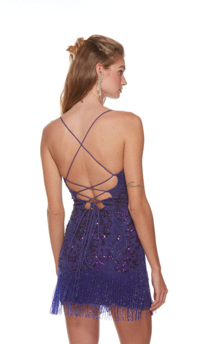 A cobalt blue short prom dress featuring a sheer corset bodice, hand beaded design throughout, and beaded fringe starting at the hip to hemline, creating a playful and fun look. The back has a thin strap lace-up enclosure for the perfect fit.