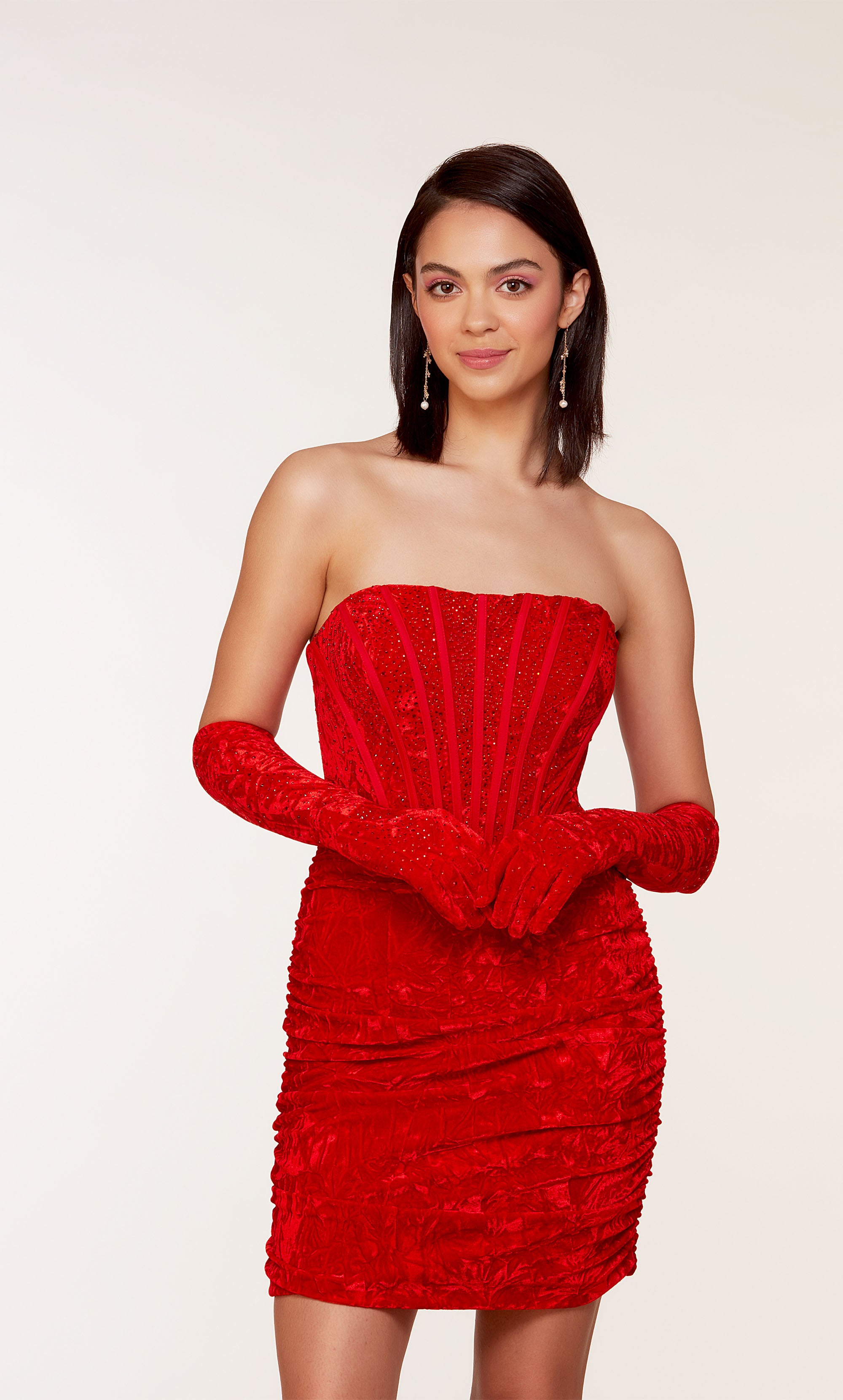 An 80's inspired red velvet corset dress with a strapless neckline and a ruched skirt. The matching gloves level up this chic look.