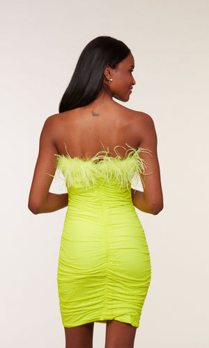 A stretch mesh strapless tube dress adorned with sparkly stones, ruching detail, and feather trim in a bright neon-green.