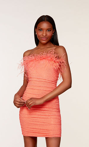 A stretch mesh strapless tube dress adorned with sparkly stones, ruching detail, and feather trim in a pretty hot coral color.