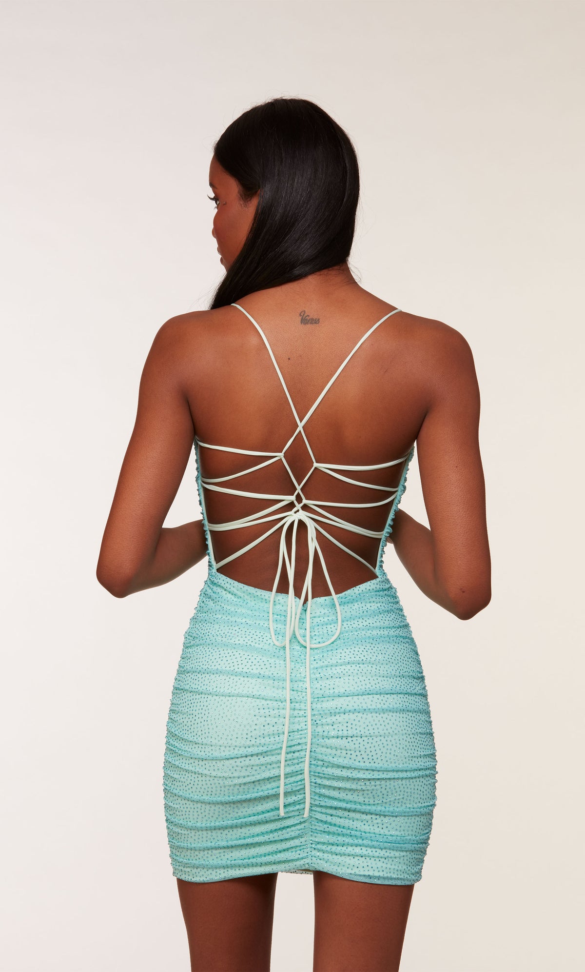 A mesh, light blue short formal dress with a strappy back, ruching detail, and heat-set stone embellishment throughout.