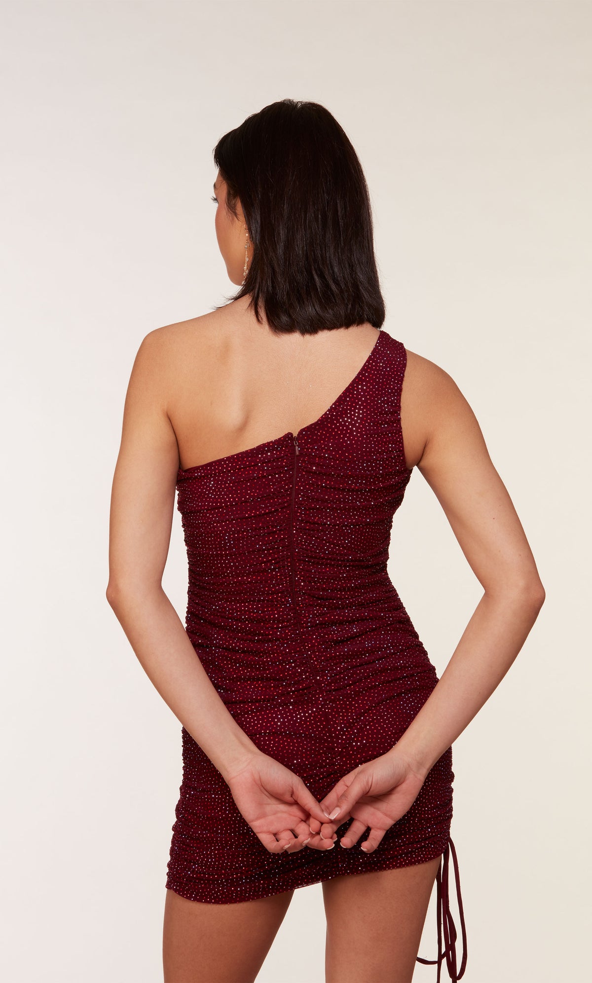 A ruched, one shoulder, short homecoming dress adorned with heat-set stones for a little bit of sparkle, in the color burgundy.