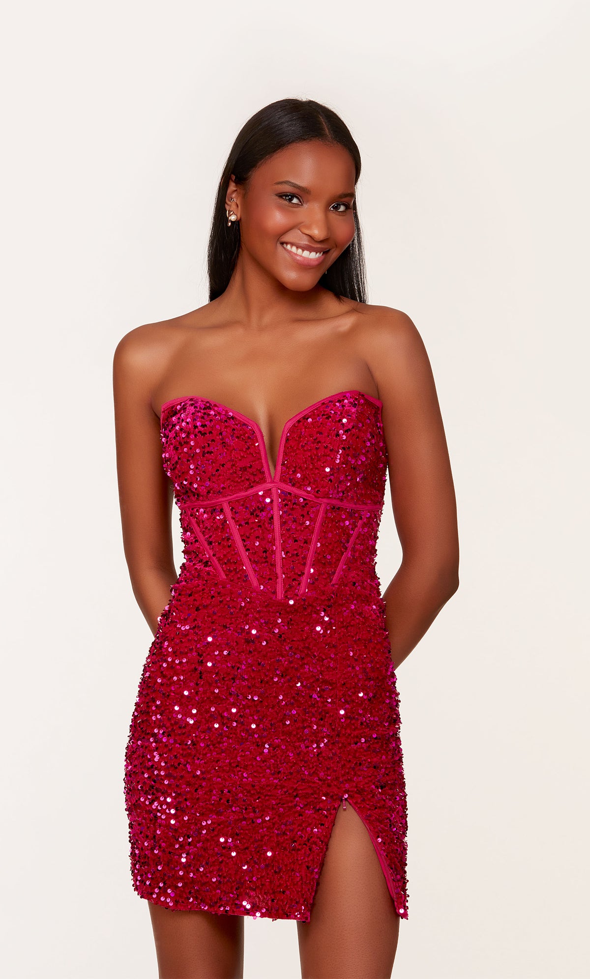 A short corset prom dress in iridescent, raspberry colored sequins. The dress features a strapless neckline, a zipper side slit, and a lace-up back.