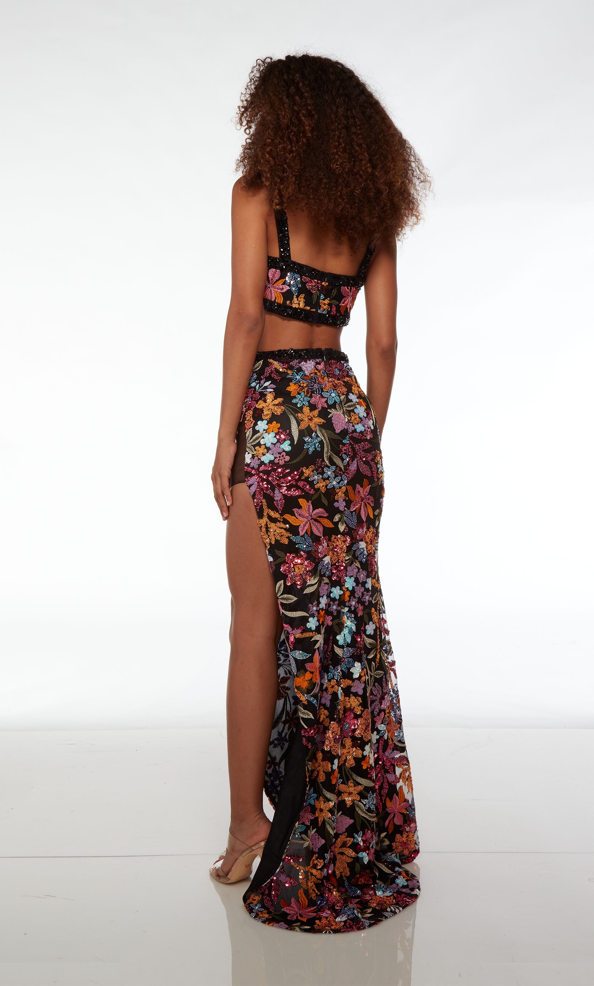 Gorgeous black two-piece dress: V-neck crop top and high-waisted skirt adorned with black rhinestone trim, high slit, slight train, and colorful sequined flowers.