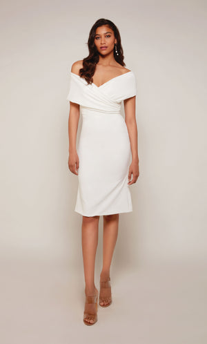 A chic, knee length cocktail dress with an off the shoulder neckline, ruching detail, and a closed zipper back in ivory.