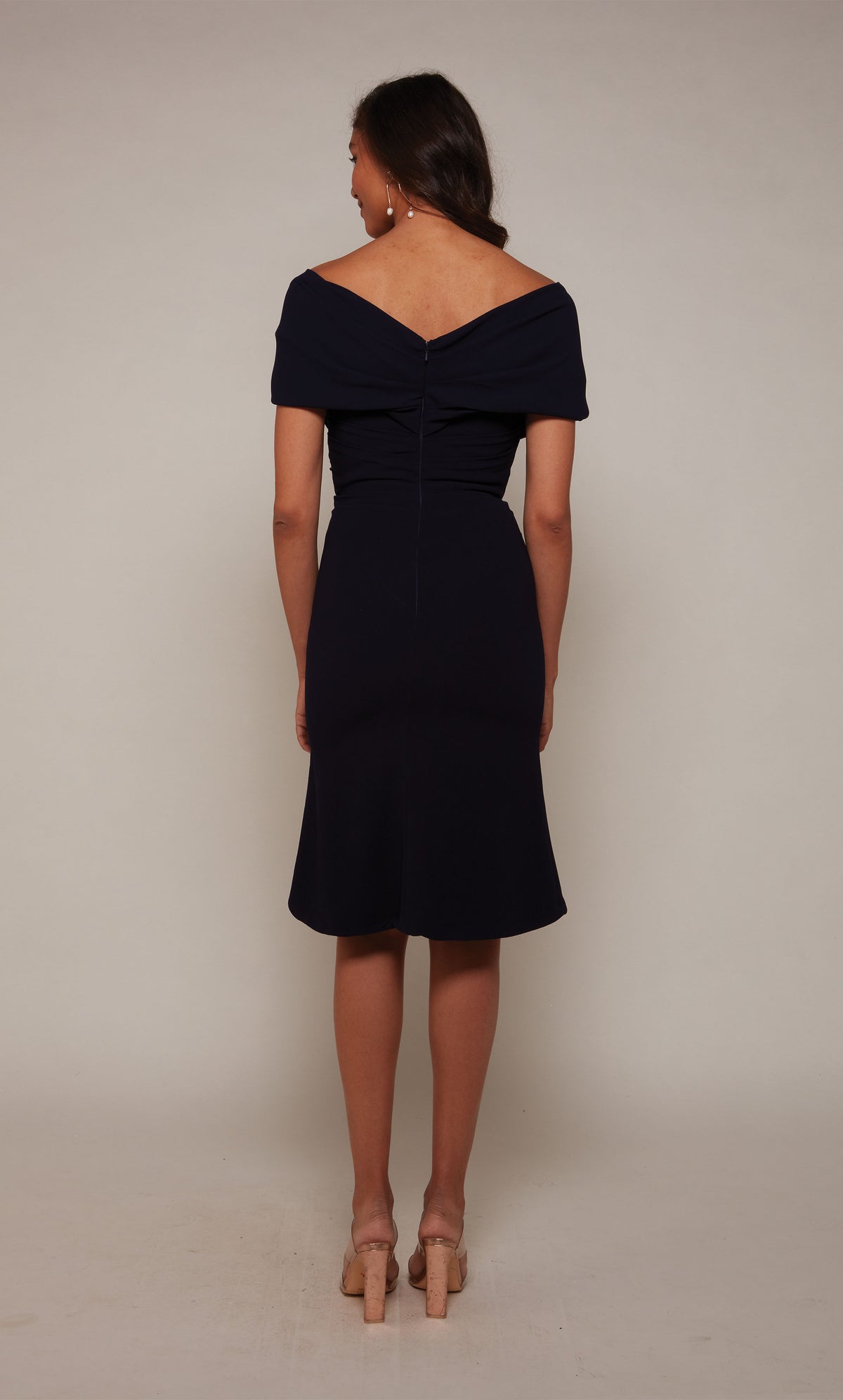 A chic, knee length cocktail dress with an off the shoulder neckline, ruching detail, and a closed zipper back in midnight blue.