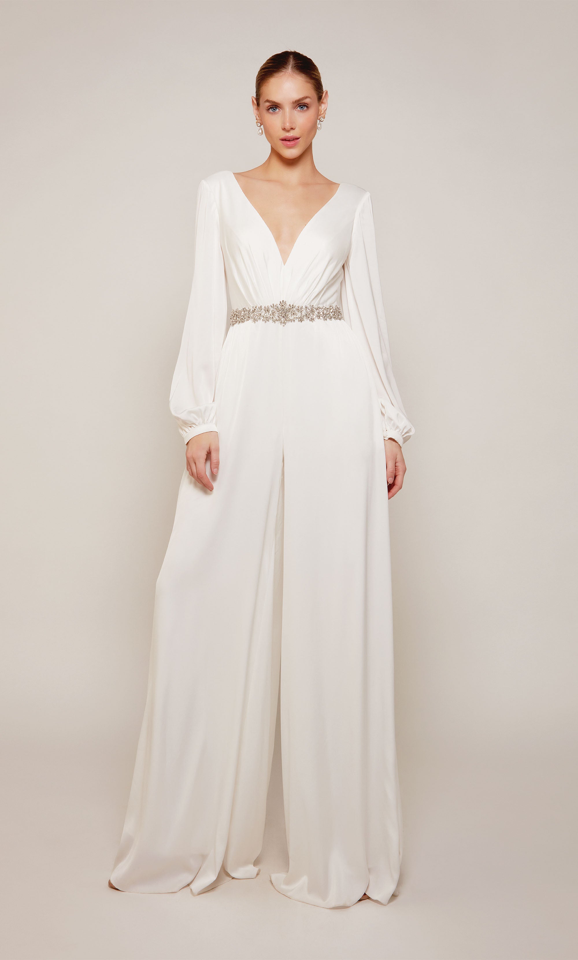 A long sleeve jumpsuit with an plunging neckline, jeweled waist, and wide leg pant in ivory. Color-SWATCH_70031__IVORY