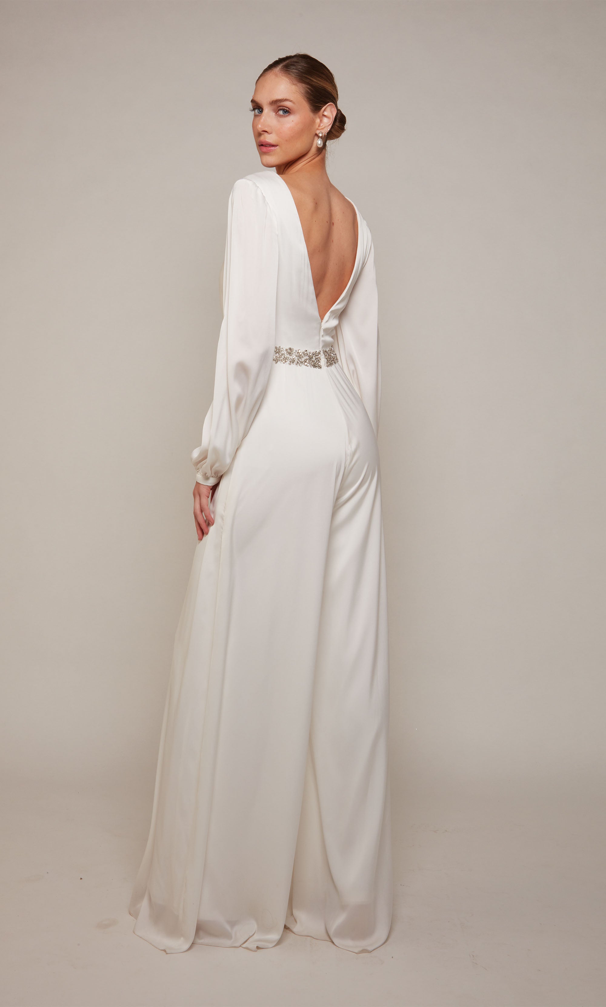 A long sleeve jumpsuit with an plunging neckline, jeweled waist, and wide leg pant in ivory. Color-SWATCH_70031__IVORY