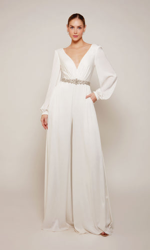 A long sleeve jumpsuit with an plunging neckline, jeweled waist, and wide leg pant in ivory.