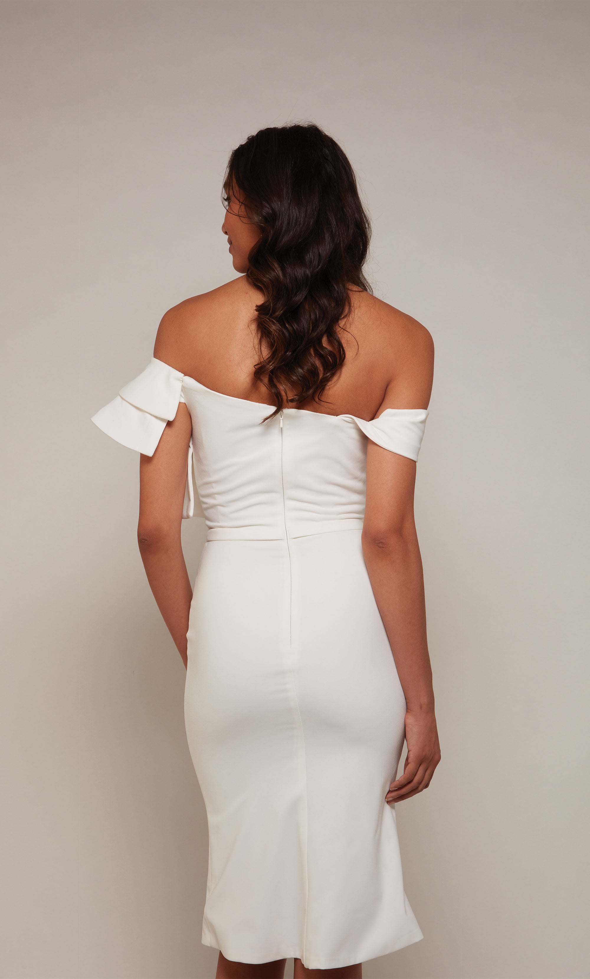 A knee length, white engagement dress with a ruffled off the shoulder neckline and faux belt at the natural waistline.