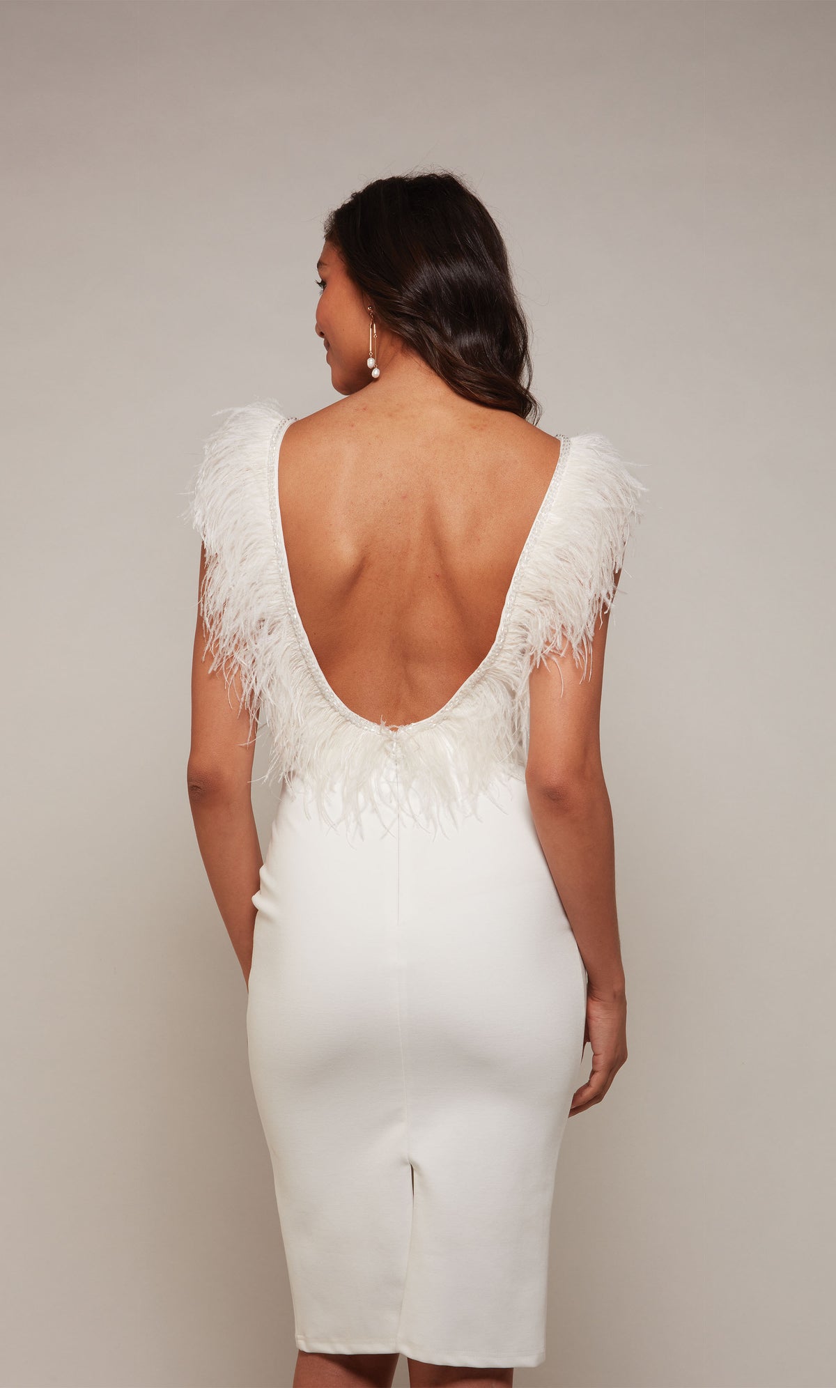 A chic, knee length cocktail dress with a U-shaped open back, a back slit, and feather trim in diamond white.