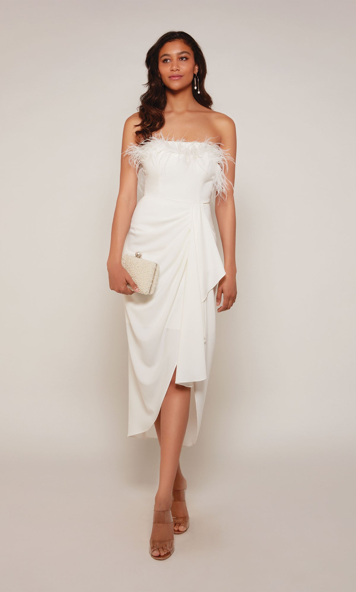 An ivory colored asymmetrical hemline dress  with a strapless neckline, feather trim, and a cascading drape in the front.