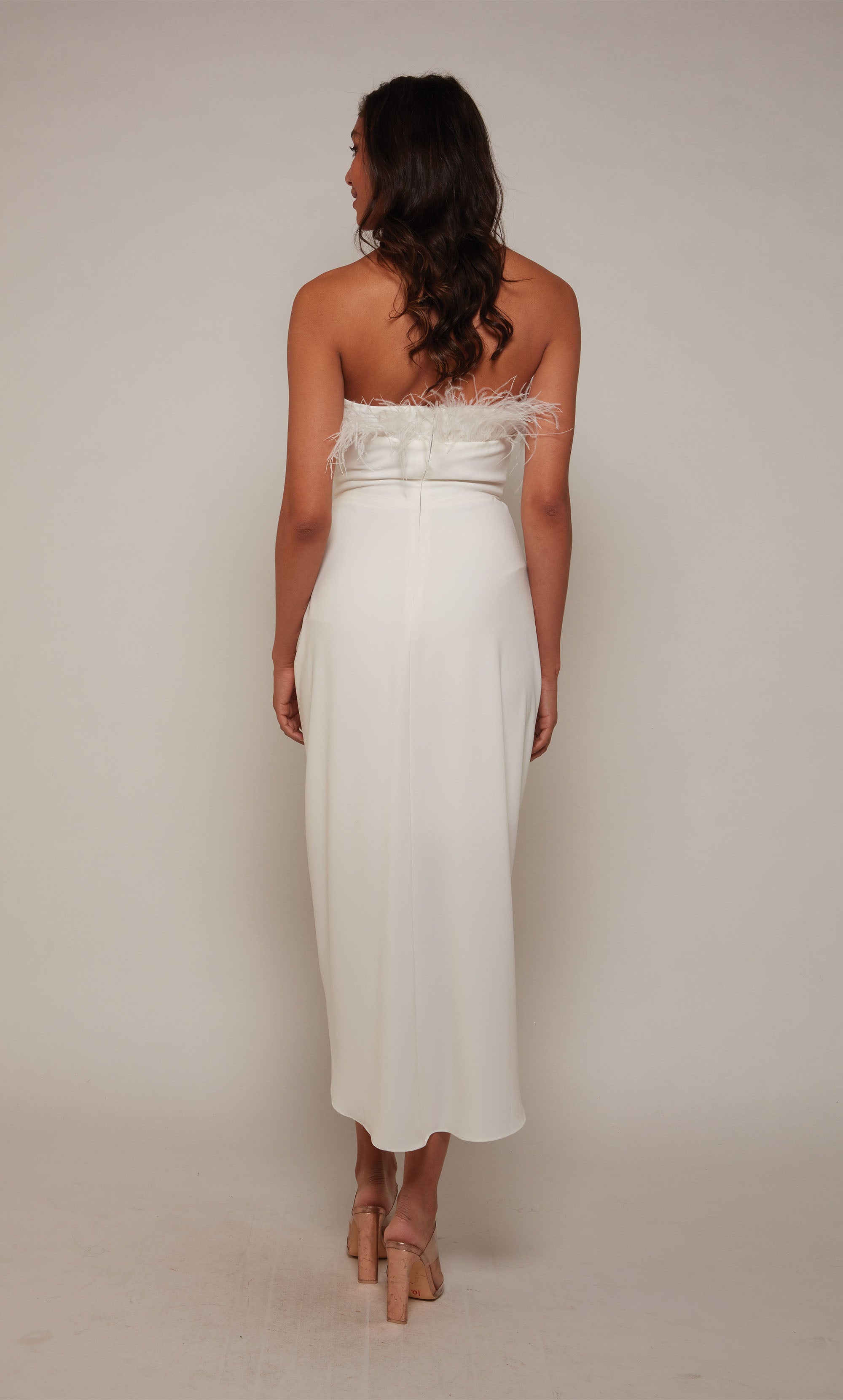 An ivory colored asymmetrical hemline dress  with a strapless neckline, feather trim, and a cascading drape in the front.