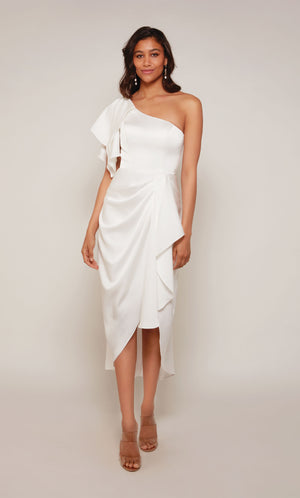 A white one shoulder cocktail dress with an asymmetrical hemline, ruffle shoulder, and cascading front drape.