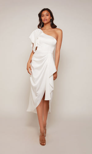 A white one shoulder cocktail dress with an asymmetrical hemline, ruffle shoulder, and cascading front drape.