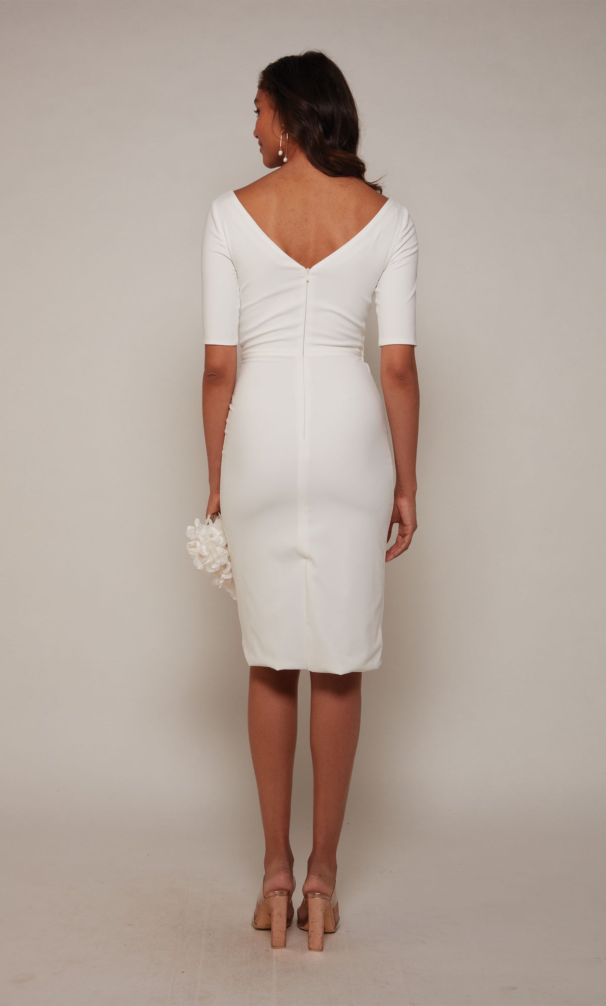 A fitted, knee length cocktail dress with a V-shaped back and 3/4 sleeves in ivory.