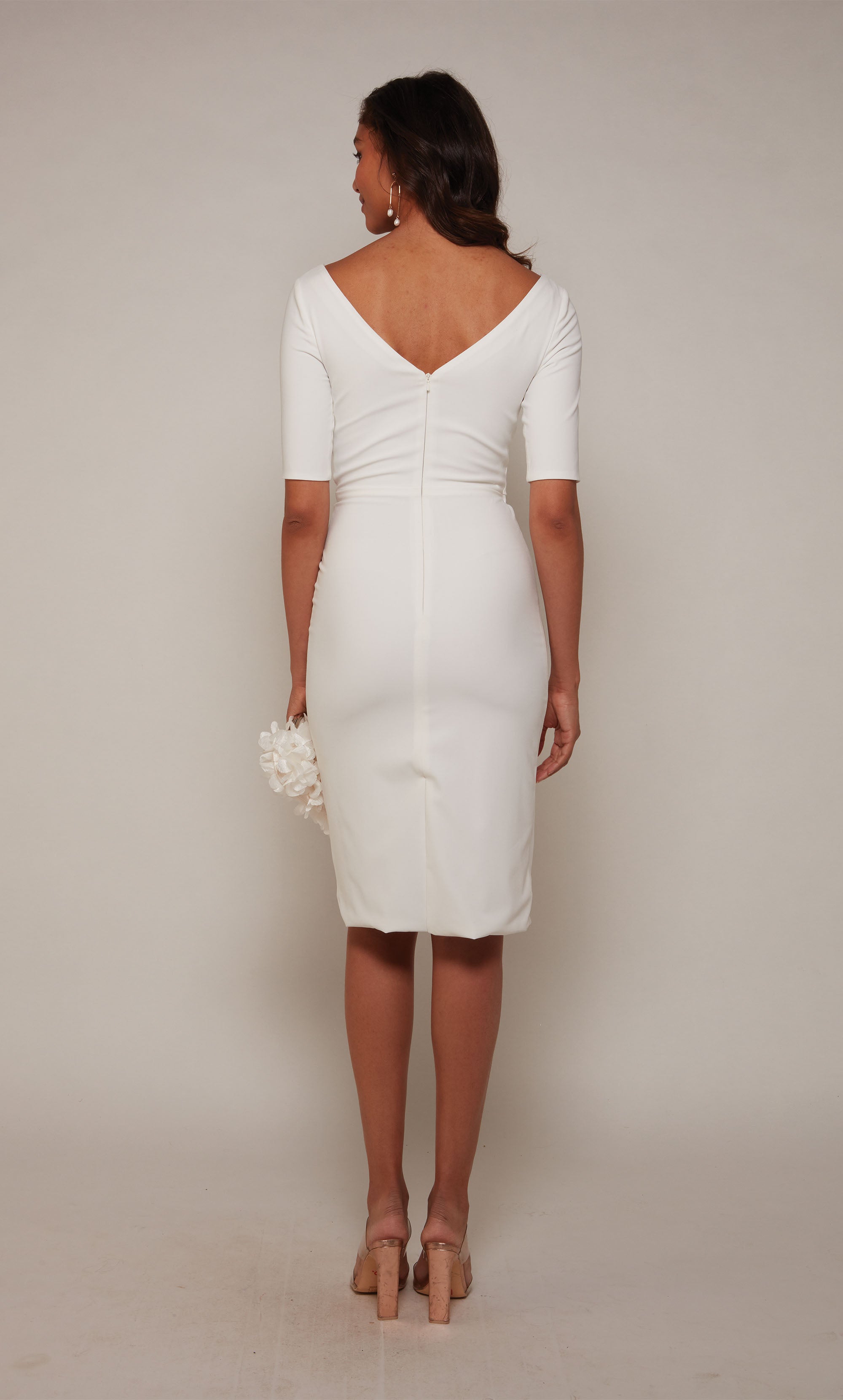 A fitted, knee length wedding dress with an off center V-neckline and 3/4 sleeves in ivory.