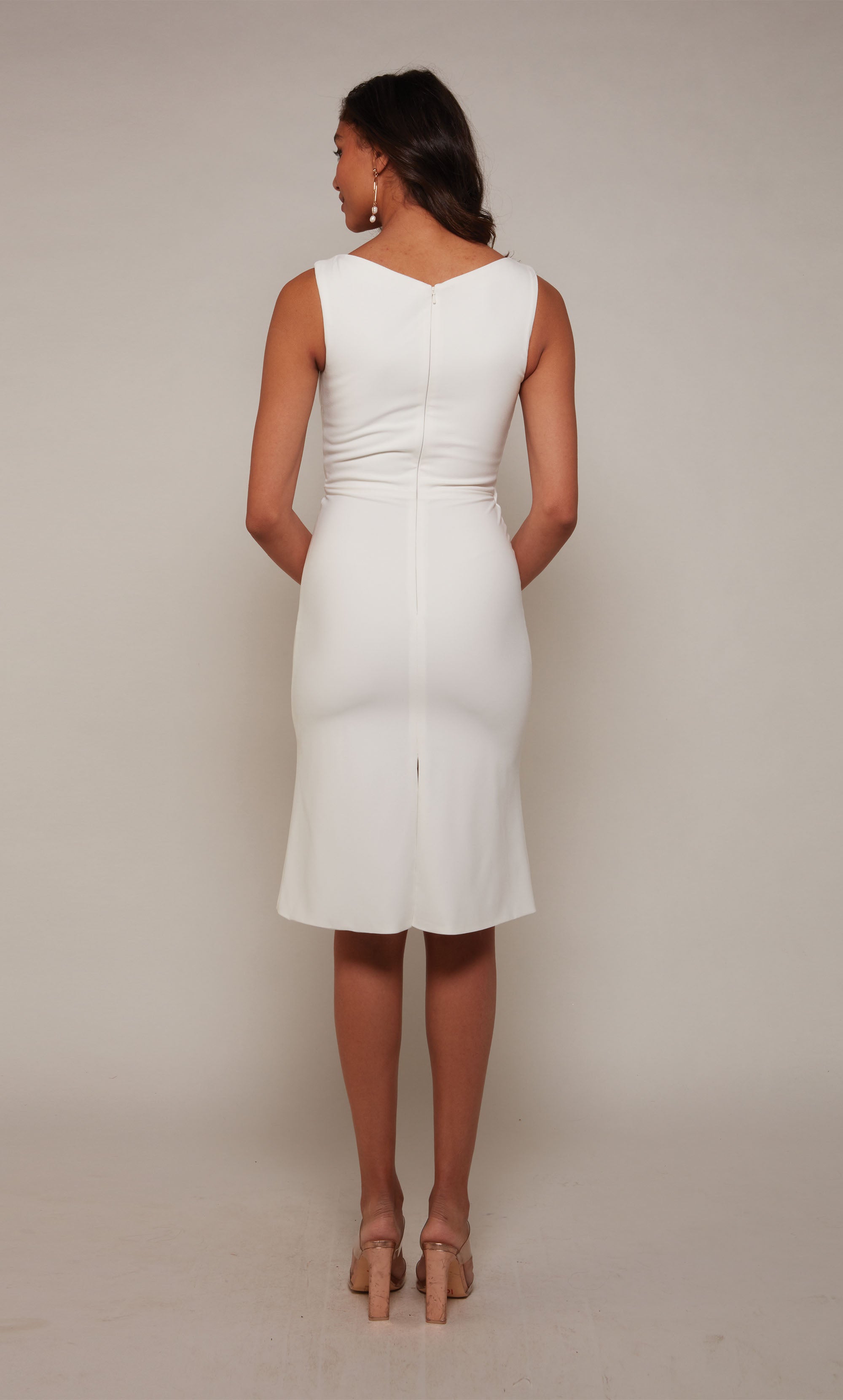 A sleeveless, ivory cocktail dress with an off center V-neckline and ruching detail. The skirt is fitted with a knee length hemline.
