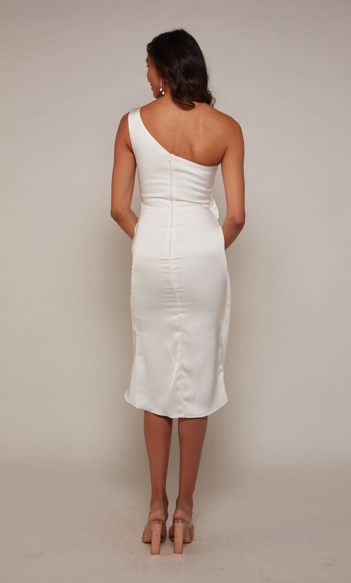 A satin wedding dress with a one shoulder neckline, a zip-up back, and an asymmetrical hemline in diamond white.