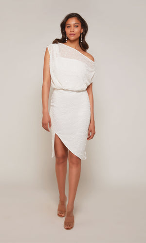A shimmery, hand beaded, ivory cocktail dress with a one shoulder neckline, a cinched waist, and an asymmetrical hemline.