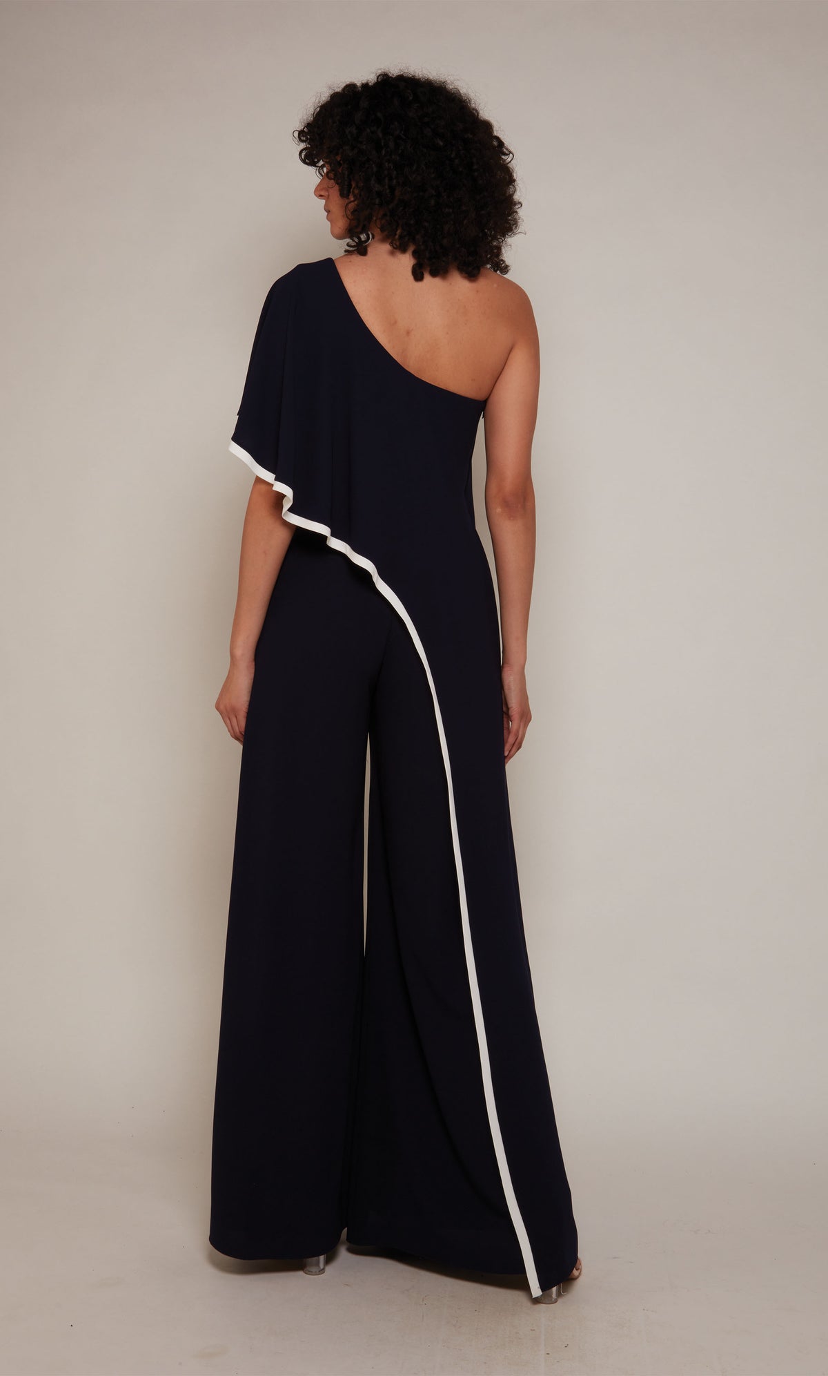 A wide leg, formal jumpsuit with a one shoulder neckline and draped bodice in navy blue with ivory trim.
