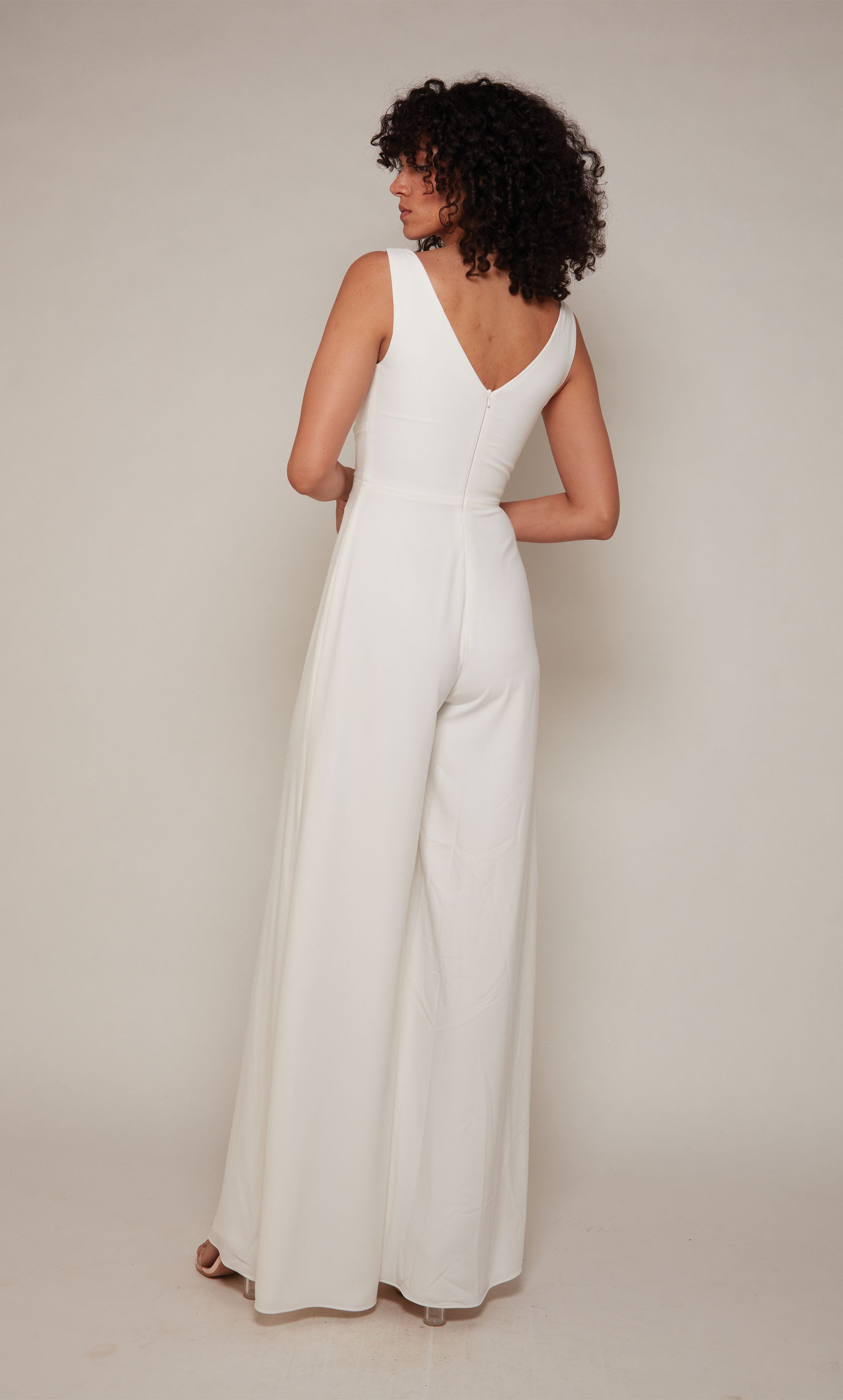 A white formal jumpsuit with an off center V-shaped neckline and wide leg pant.