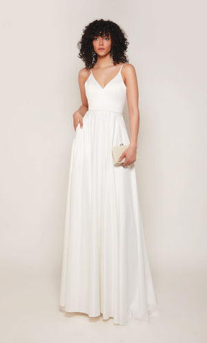A simple, satin wedding dress with a V-neckline, an A-line skirt complete with pockets, a pearl accented waistline, and a V-shaped open back with satin covered buttons cascading down the back to the tip of the elegant train.