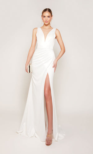 A white, satin wedding gown featuring a plunging illusion neckline, pleated skirt below the waistline, and elegant side slit.